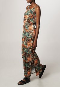 Robe maxi avec un motif de plumes de paon dans des teintes orange, verte et brune. Tissu léger avec une coupe décontractée et des fentes sur les côtés.