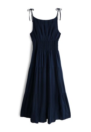 Varrukateta tumesinine midi-kleit astmelise seelikuga, soonikkoes vöökohaga ja õhukeste õlastriipudega, mis on valgel taustal paeladega seotud.