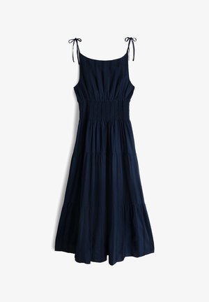 Αμάνικο μεσάτο φόρεμα σε ναυτικό μπλε με φούστα σε στρώσεις, σφηκοφωλιά στη μέση και λεπτές τιράντες στους ώμους δεμένες σε φιόγκους σε λευκό φόντο.