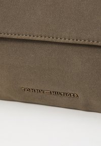 Sac kaki avec un tissu texturé. Doté d'un logo doré en relief "TOMMY HILFIGER" à l'avant et d'un design épuré et minimaliste.