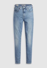 Jeans slim bleu clair avec fermeture par bouton et zip, poches avant et arrière, et légère décoloration sur les cuisses, présenté sur un fond uni.