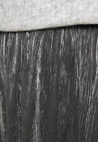 Metallic plisserad kjol med svart bas, som har iriserande vertikala ränder och en mjuk grå stickad midjeband. Texturerad yta är synlig.