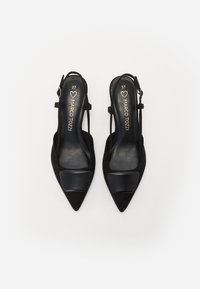 Zapatos de tacón negro tipo slingback con puntera afilada, material de ante y detalles en negro brillante en la caja del dedo. Cuenta con una delicada correa en el tobillo. Talla 37.