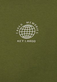 T-shirt verde oliva con testo stampato bianco che recita "Memorie Sbiadite" sopra un design del globo e "Key Largo" sotto in un carattere in grassetto. Texture morbida.