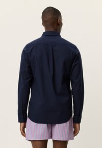 Μακρυμάνικο πουκάμισο σε ναυτικό μπλε χρώμα από βαμβάκι, με γιακά που κουμπώνει και κουμπωμένα μανίκια, συνδυασμένο με ροζ και λευκές ριγέ βερμούδες.