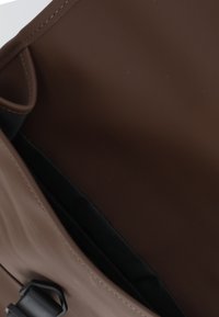 Interior de bolsa impermeable marrón con forro de tela texturizada, presenta un cierre superior con herrajes y detalles de costura suaves.