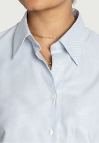 Camicia azzurra a righe sottili con colletto classico, dotata di bottoni bianchi e una texture liscia. Dettagli rilevanti includono un colletto stratificato.