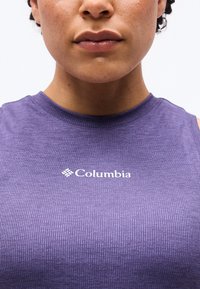 Gros plan sur une personne portant un haut sans manches côtelé violet avec un logo blanc Columbia centré sur la poitrine.