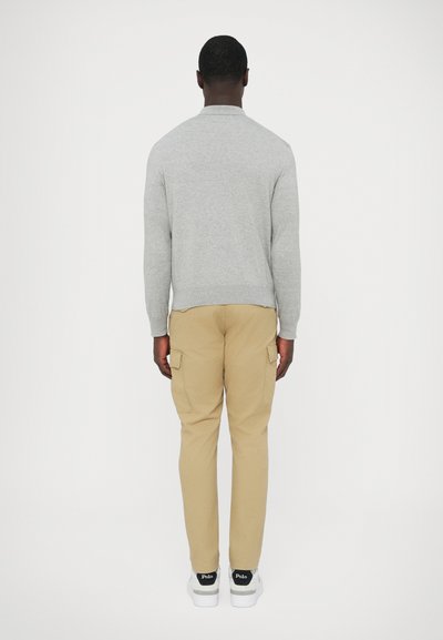 Szürke hosszú ujjú ing, khaki színű cargo nadrág oldalzsebekkel, fehér sportcipő fekete részletekkel, hátulnézetben.