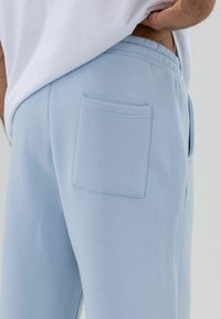 Pantalon de survêtement bleu clair en mélange de coton, avec une ceinture élastique, des poches latérales dans les coutures et une poche carrée à l'arrière.