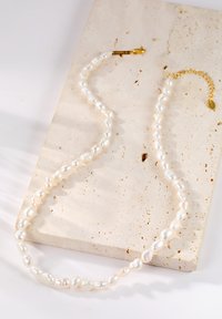 Collar de perlas de agua dulce con perlas blancas de forma irregular, asegurado con un cierre y cadena en tono dorado para longitud ajustable.
