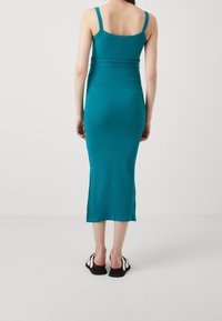 Teal gestreiftes Midi-Kleid mit dünnen Trägern und figurbetonter Silhouette, mit einem Taillenbund-Detail und geradem Saum, kombiniert mit schwarzen Slippers.
