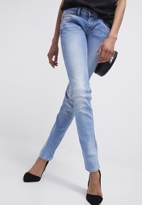 Světle modré skinny džíny vyrobené z denimu s vybledlým povrchem, štíhlý silueta, design s pěti kapsami, nasazené s černými podpatky.