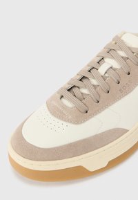 Sneaker alb și bej cu un upper din piele netedă și suede, vârf rotund, talpă texturată și șireturi plate cu detalii de brand embosate.