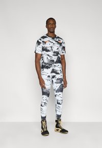 Αθλητικό πουκάμισο και κολάν με ασπρόμαυρο μοτίβο από ελαστικό ύφασμα, συνδυασμένα με μαύρα και χρυσά ψηλά παπούτσια.