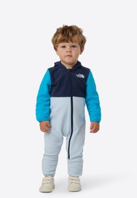 Jednoczęściowy kombinezon polarowy z zamkiem błyskawicznym, granatową górą, jasnoniebieskim dołem i turkusowymi rękawami; posiada kaptur i wytrzymałą tkaninę.