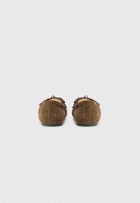 Brune mokkasinslippers i semsket skinn vises fra baksiden, med en rund tupp og et dekorativt belte med spenne.