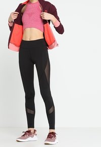 Completo da attrezzatura sportiva composto da un top corto fittato rosa, leggings neri con accenti in rete e scarpe da ginnastica rosse e bianche.