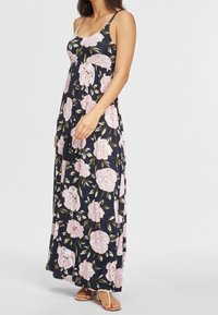 Sukienka maxi z granatowym tłem, ozdobiona dużymi różowymi wzorami kwiatowymi i zielonymi liśćmi. Cienkie ramiączka i luźny krój.