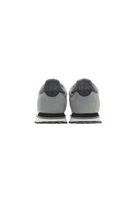Un paio di sneakers grigie viste da dietro, con tab posteriori neri su cui è stampato in grigio "Dal 1890".