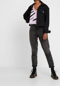 Czarna dżinsowa kurtka, jasnofioletowy crop top w czarne paski, szare spodnie z wysokim stanem oraz czarne lace-up buty. Codzienny strój z kontrastującymi kolorami.