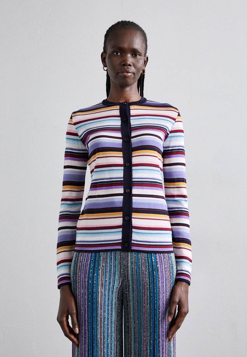 Bunt gestreifter Cardigan mit horizontalen Mustern in unterschiedlichen Breiten, ausgestattet mit einer dunkelblauen Knopfleiste und einem gerippten Kragen. Kombiniert mit gestreiften Hosen.