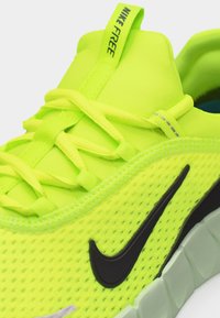 Chaussure de course Nike Free jaune vif avec logo swoosh noir, tige en mesh, lacets et languette avec tirette.