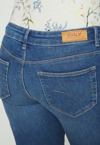 Vaqueros azul oscuro con un diseño ajustado, que cuentan con bolsillos traseros, un patrón cosido y una etiqueta de cuero marrón con la palabra "ONLY" en la cintura.
