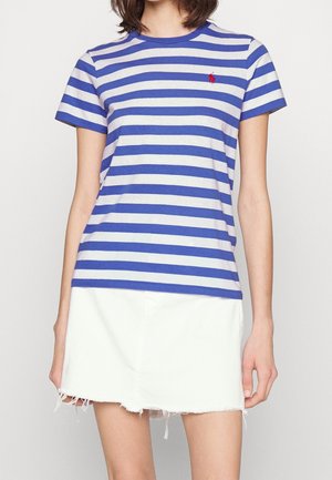 Frau trägt ein blau-weiß horizontal gestreiftes Kurzarmshirt und einen weißen, ausgefransten Minirock.