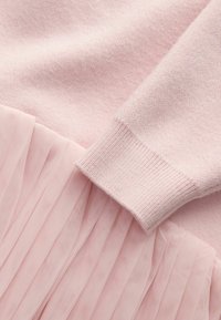 Svetloružový sveter s textúrovanou látkou na vrchu a vrstvenou plisovanou tylovou sukňou na spodku, s rebrovanými manžetami.