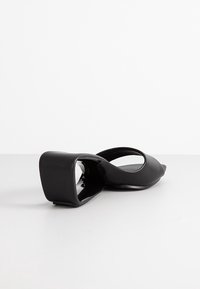 Scarpa nera open-toe con un design elegante, caratterizzata da un retro chiuso e un tacco a blocco angolare. Realizzata in materiale liscio e lucido.