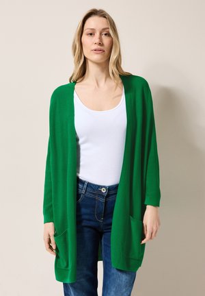Green open cardigan with long sleeves, made of knit material. Features two front pockets and a relaxed fit over a white top and denim jeans.