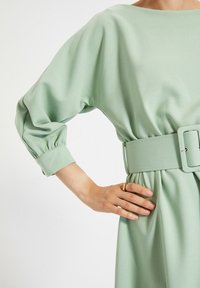 Jasnozielona sukienka do kolan z marszczoną talią, szerokimi rękawami i szerokim paskiem. Miękka tekstura z gładkim wykończeniem.