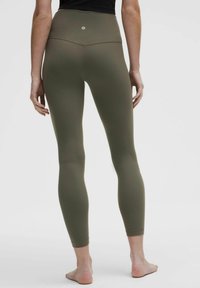 High-waisted, olive green leggings with a smooth texture and fitted design. Features a small logo at the back and tapered ankles.