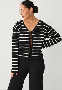 Zwart-witte gestreepte gebreide cardigan met een V-hals, lange mouwen en een striksluiting aan de voorkant. Zachte textuur en een relaxte pasvorm.