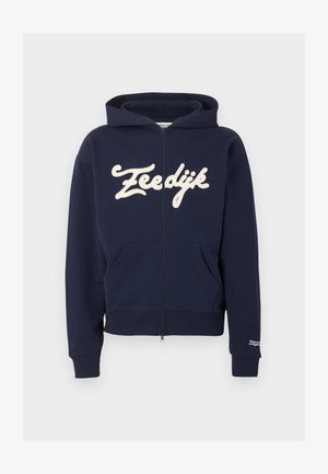 Marineblauer Kapuzenpullover mit Reißverschluss, Vordertaschen, gerippten Bündchen und Saum, cremefarbener Schriftzug "Zeedijk" über der Brust und kleinem weißen Text am Bündchen des linken Ärmel.