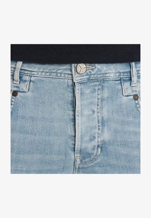 Lichtblauwe lichtgewassen spijkerbroek met een zilveren knoop en zichtbare stiknaden onder een zwart geribd topje.