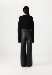 Pull noir en grosse maille avec manches longues, associé à un pantalon en cuir noir taille haute, à jambes larges. Design minimaliste, sans motifs visibles.