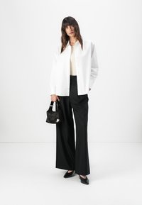 Oversized white button-up shirt, beige top, wide black trousers, black heels, and a small black handbag with a silver accent.