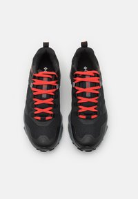 Czarne sportowe buty z teksturowaną cholewką, czerwonymi sznurówkami i szarymi akcentami. Posiadają amortyzowaną podeszwę i wzmocniony obszar palców.