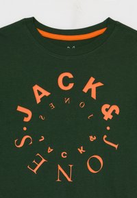 Temno zeleni bombažni T-shirt z okroglo oranžno besedilno zasnovo. Okroglo izrezan ovratnik z kontrastnim oranžnim notranjim robom.