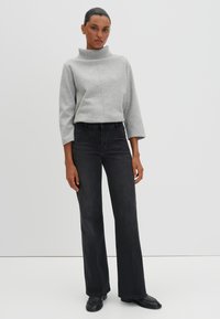 Pull gris avec un col haut, des manches mi-longues et un détail de couture, associé à un jean noir évasé et des chaussures noires.