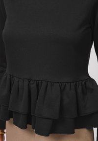 Top negro de manga larga con dobladillo con volantes de múltiples capas, confeccionado en una tela suave y elástica. La textura es suave y elegante.