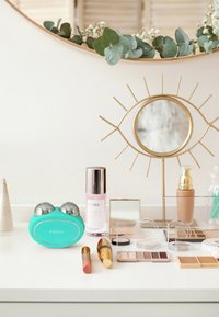 Dispositif de soin de la peau turquoise avec accents métalliques, flacon de sérum rose, divers cosmétiques, miroir doré et verdure dans un cadre moderne.