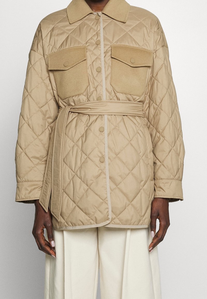 Veste matelassée beige avec un col, deux grandes poches à rabat et une ceinture à la taille. Texture lisse avec un passepoil contrastant plus clair.