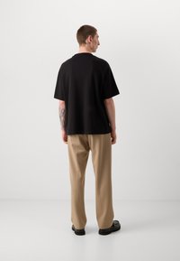 Black short-sleeve t-shirt with a relaxed fit, paired with beige trousers. The t-shirt features a simple, smooth texture and crew neckline.
