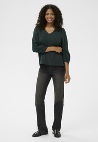 Donkergroen V-hals pullover met driekwartmouwen en gathered manchetten, gecombineerd met zwarte rechte jeans en zwarte loafers.