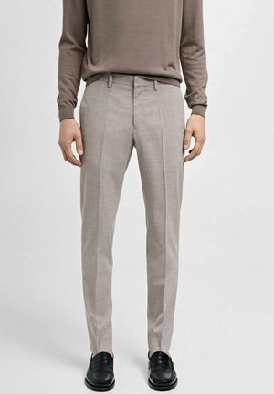 Světle šedé kalhoty na míru s vertikálními pruhy, texturovaná látka a slim fit. Nosené s hnědou košilí s dlouhým rukávem a černými botami.