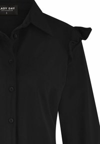 Zwarte lange mouwen blouse met knoopsluiting, puntkraag en kleine ruches op de schouder, maat small van Lady Day Amsterdam.