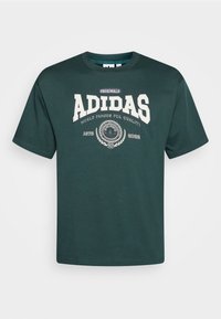 Camiseta de Adidas Originals en verde oscuro con el texto del logo en blanco "Famoso en el mundo por su calidad" y "1972 2022" celebrando 50 años.